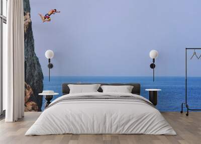 Young man jumping off cliff into blue water ocean at sunset. Active outdoor, holiday adventure, tourism action, healthy summer joy, Fun activity lifestyle. Crazy adult guy in swimwear fly from climb. Wall mural