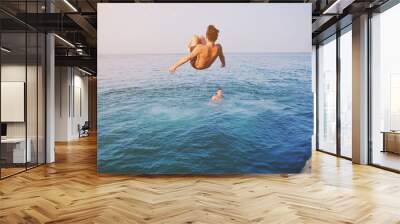 Young man jumping off cliff into blue water ocean at sunset. Active outdoor, holiday adventure, tourism action, healthy summer joy, Fun activity lifestyle. Crazy adult guy in swimwear fly from climb Wall mural