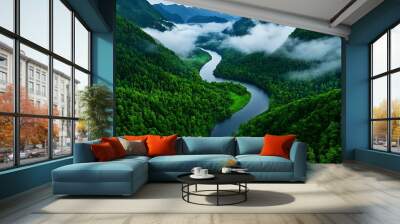 An aerial view of a river meandering through lush green forests and fog-covered mountains. Wall mural