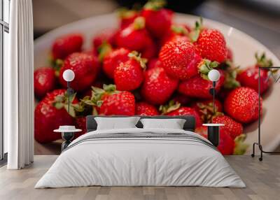 A close-up of fresh, ripe strawberries piled in a bowl, showcasing their vibrant red color and green leaves. Wall mural