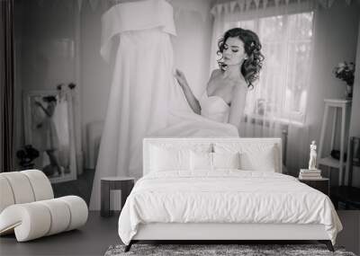 Valmiera, Latvia - September 9, 2023 - Bride holding her white wedding dress in a room with a large window and mirror, captured in black and white. Wall mural