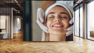 Close up of hands of young cosmetologist injecting botox in female face. She is standing and smiling. The woman is closed her eyes with relaxation Wall mural