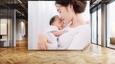 Asian mother holding her newborn in arm and sleeping together with love and care, adorable baby in mom arm sleeping with happy and safe, infant and mother concept. Wall mural