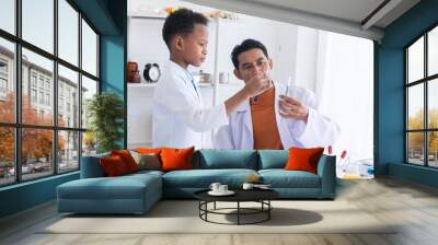 Cheerful African boy and Indian teacher with mustache wearing lab coat uniform studying science class in laboratory, pupil boy show test result to scientist professor with stethoscope and test tube Wall mural