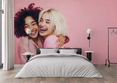 Two young women are having fun and friends are hug over pink background Wall mural