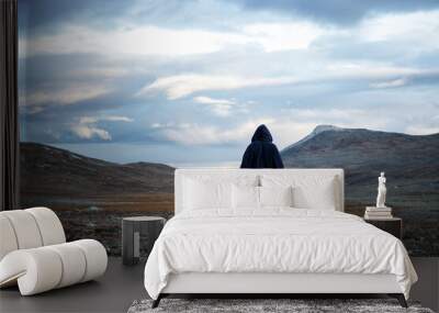 Back view silhouette of traveler man standing on the mountain.  A mysterious cloaked man. Medieval man in hooded cloak. Wall mural