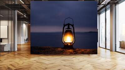 Beautiful old rustic oil lamp silhouette on the rock in a beautiful sea backgroud. Night time. Light in the dark and hope concept.  Wall mural