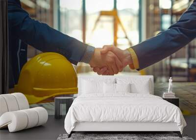 yellow safety helmet on workplace desk with construction worker hands shaking project contract in office at construction site Wall mural