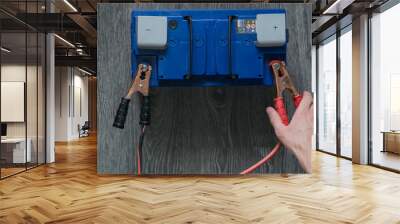 The male hand connects the terminals to the car's batteries on a wooden background Wall mural