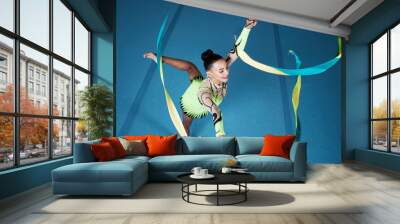 Rhythmic gymnastics, woman in gym and ribbon with balance, action with performance and fitness. Competition, athlete and female gymnast, creativity and art with dancing routine and energy at arena Wall mural