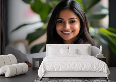 A beautiful Indianmanager  woman wearing formal attire smiles while reading documents in her office Wall mural