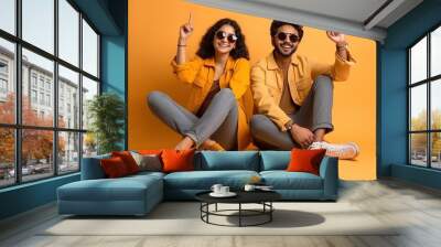 Indian couple sitting on the floor wearing jeans and sunglasses Wall mural