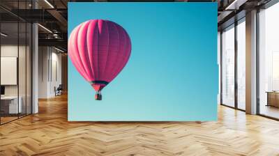 A vibrant pink hot air balloon floats against a clear blue sky, symbolizing adventure and leisure. Wall mural