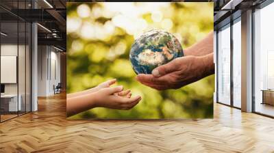 Close up of senior hands giving small planet earth to a child over defocused green background with copy space Wall mural