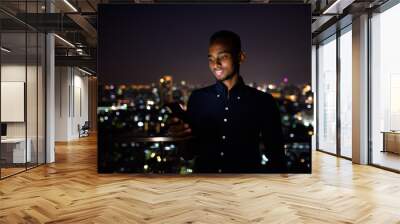 Happy African businessman outdoors at rooftop using phone at night Wall mural