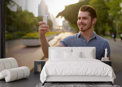 Happy man relaxing at the park while using mobile phone Wall mural