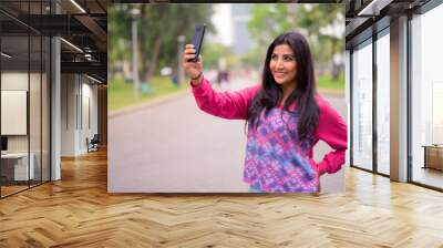 Happy young beautiful Persian woman taking selfie at the park Wall mural