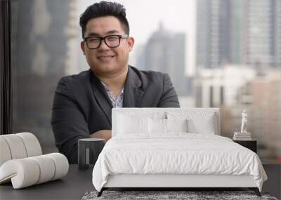 Happy young overweight Asian businessman against view of the city Wall mural