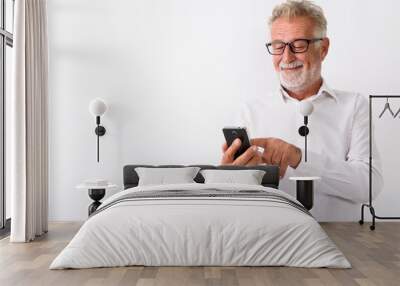 Studio shot of happy senior bearded man smiling while using mobi Wall mural