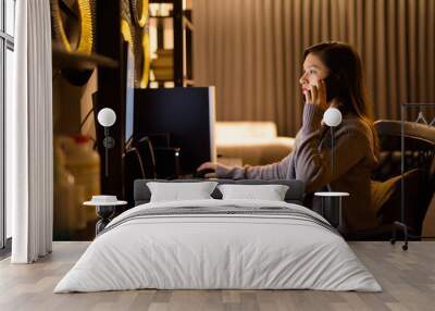 Young Asian woman talking on the phone while working from home Wall mural