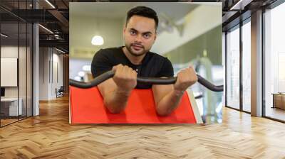 Young bearded Indian man lifting weights at the gym Wall mural