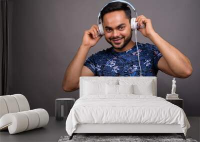 Young bearded Indian man listening to music against gray backgro Wall mural