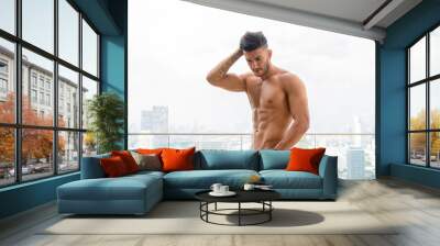 Young handsome muscular Persian man shirtless and looking down against view the city Wall mural