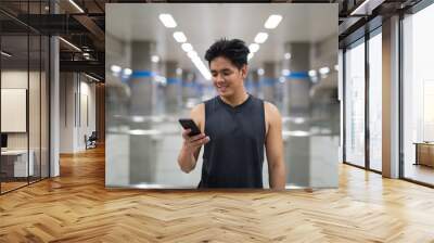 young happy asian man using phone at the subway station Wall mural