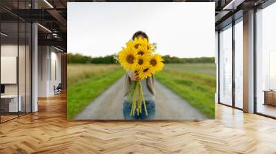 Young woman giving sunflowers against view of the field in nature Wall mural