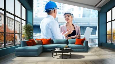 Business engineer Men and women standing and talking meeting is on job site. Wear blue and white helmet for safety. Use the laptop to enter into an agreement to participate in construction business Wall mural