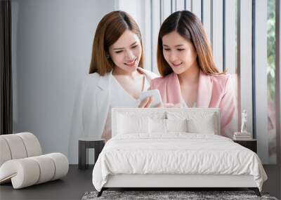 Two women are watching holding the smartphone. Which is reading news in the world today. And the order of online clothes fashion shopping. And communicate with people around the world through the app. Wall mural