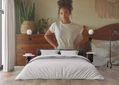 Young woman poses confidently in casual attire within a cozy, well-decorated bedroom featuring natural elements and warm lighting. Wall mural