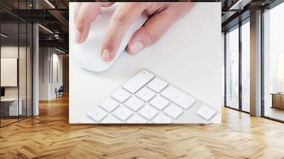 male hand clicking on a white mouse with a white keyboard on the right. White table in a office Wall mural