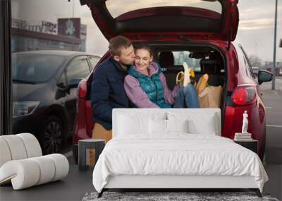 Happy couple sitting at car trunk after shopping Wall mural