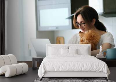 The young woman is working remotely. Young woman with her dog working using a laptop at home. Concept of the workplace at home, working remotely. Wall mural