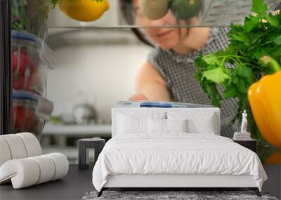 Woman looking inside a fridge full of food and choosing a salad in the container. Wall mural