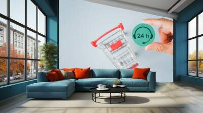 human's hand holding 24 h. call center symbol on round green paper cut with blurred shopping cart, delivery service, question, information center, shopping online, or chat with staff Wall mural