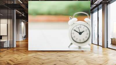 white alarm clock on desk with blurred garden background for time passing, punctuality, deadline, business countdown concept Wall mural