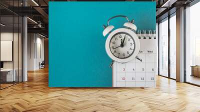 white analog alarm clock on blurred calendar with grunge blue background with copy space, business meeting schedule, travel planning or project milestone and reminder concept Wall mural