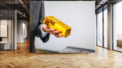 Businessman in suit sits at his desk, holding a shining gold bar. financial charts, the scene symbolizes wealth, investment success, growing influence of cryptocurrency and blockchain. Wall mural