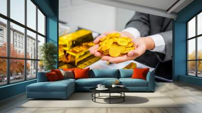 Businessman in suit sits at his desk, holding a shining gold bar. financial charts, the scene symbolizes wealth, investment success, growing influence of cryptocurrency and blockchain. Wall mural