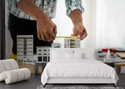 Close up Asian individual architect or engineer holding building scale model of multi-story building. design or review of architectural plans laid out on work surface in front of them. Wall mural