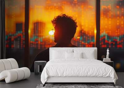 A man is standing in front of a window with a city skyline in the background. The sun is setting, casting a warm glow over the scene. The man is wearing glasses and he is looking out the window Wall mural