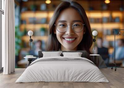 Smiling young Asian businesswoman wearing glasses in a modern office setting, embodying professionalism and confidence. Wall mural