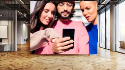 man holding a mobile phone sharing a moment with two female friends, focus on the phone, concept of technology of communication and connectivity in a digital world Wall mural