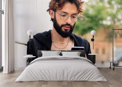 portrait of a stylish young man with beard leaning in a white wall typing on mobile phone, concept of urban lifestyle and technology of communication, copy space for text Wall mural