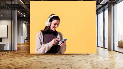 smiling young woman listening to music from phone on headphones with yellow background, concept of rhythm and positive people, copy space for text Wall mural