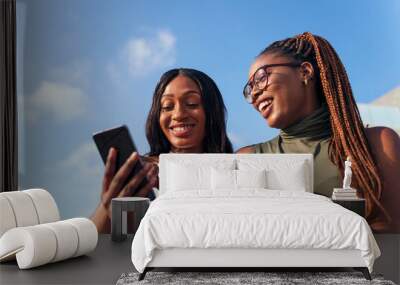 two young african women having fun looking phone Wall mural