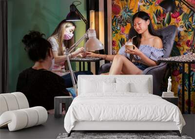 young asian woman receiving manicure and pedicure treatments at the same time while drinking a coffee in the beauty salon, wellness and body care concept Wall mural