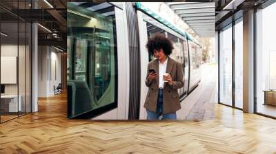 young business woman checking her phone while waiting for the tram to arrive, concept of technology and urban lifestyle Wall mural